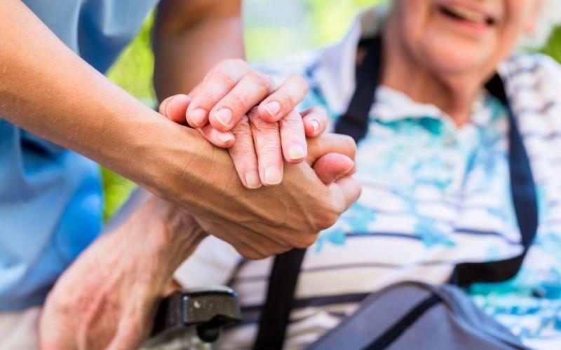 Close-up of a person holding an elderly person's hand outdoors