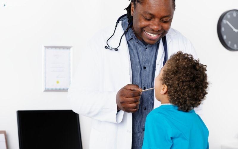 Doctor examining a child's ear with a stethoscope in a medical setting.
