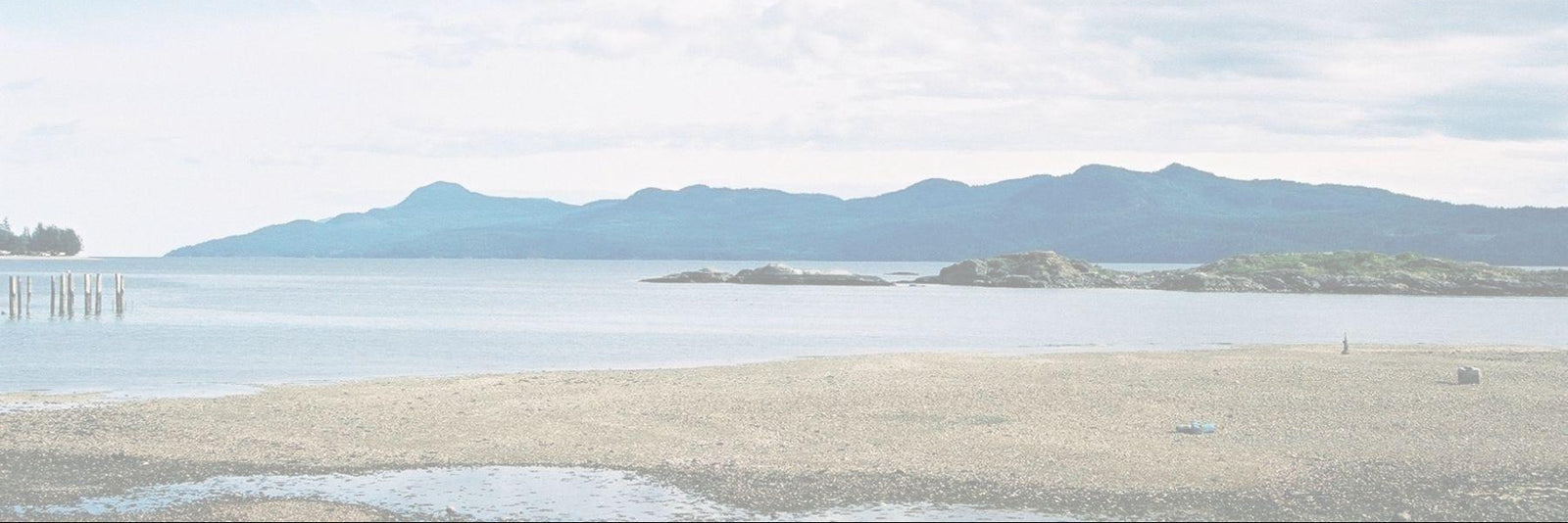 Coastal landscape with mountains in the distance under a cloudy sky.