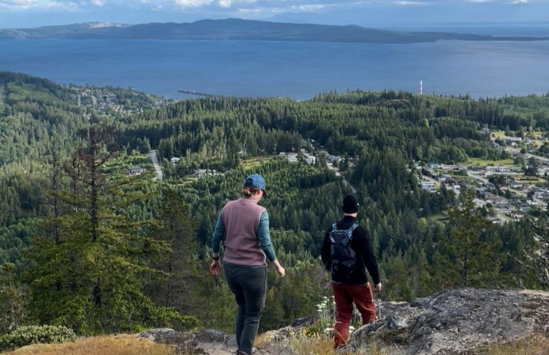 Two people hiking a mountain overlooking Powell River and the ocean.